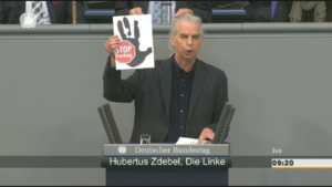 MdB Hubertus Zdebel hält am Rednerpult im Bundestag ein Stop-Fracking-Logo hoch
